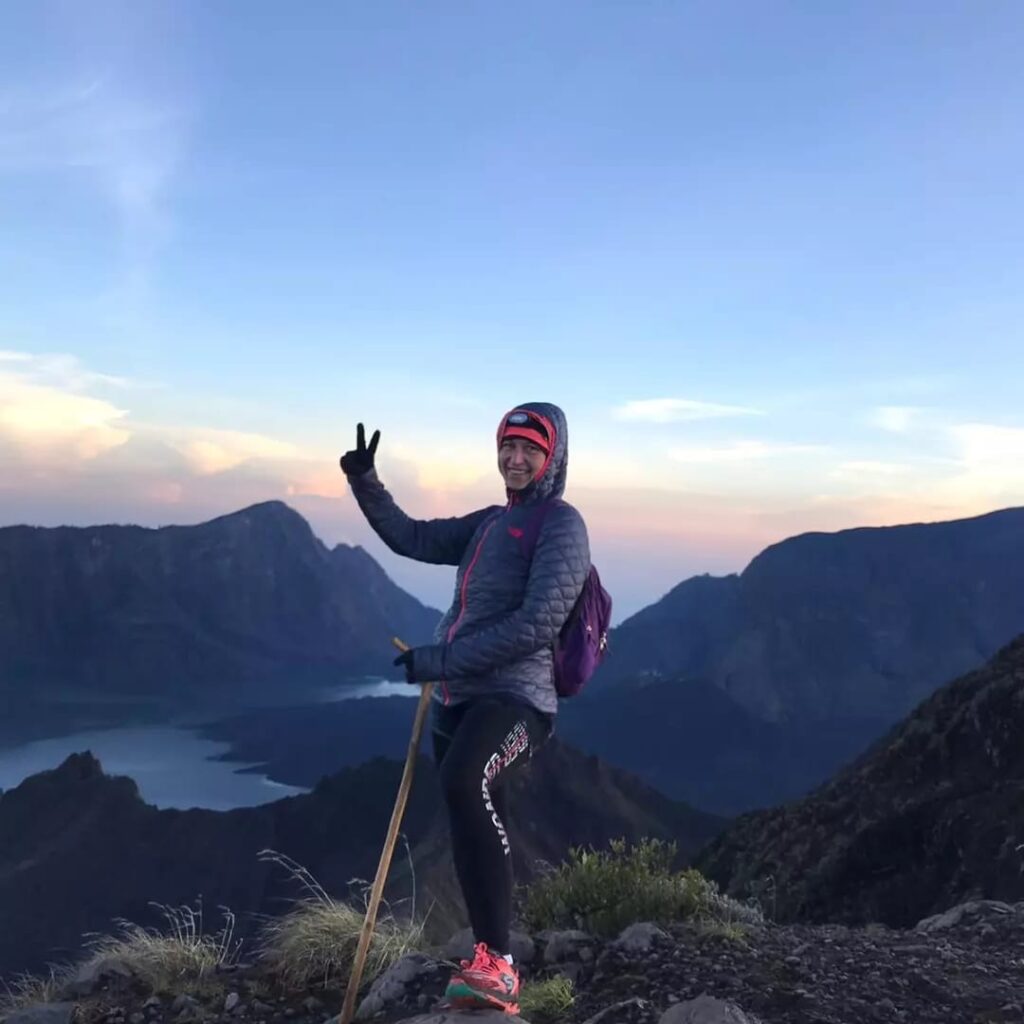 A woman standing on a mountain with a pole and a peace sign during a Lombok private tour.
