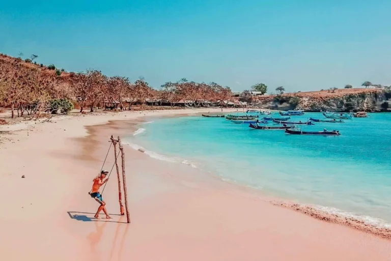 Traveler swinging on the picturesque Pink Beach of Lombok with traditional boats in the background, from our Pink Beach snorkeling tour